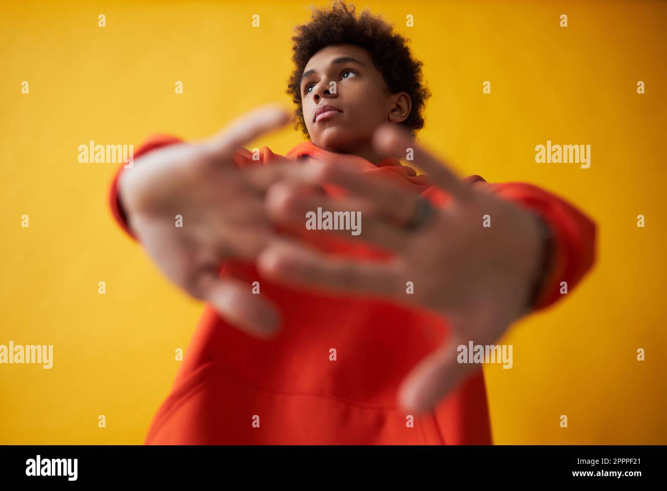 Süßer afroamerikanischer Teenager im roten Hoodie, der sich die Arme vor sich streckt und während der Fotosession auf gelbem Hintergrund posiert Stockfoto