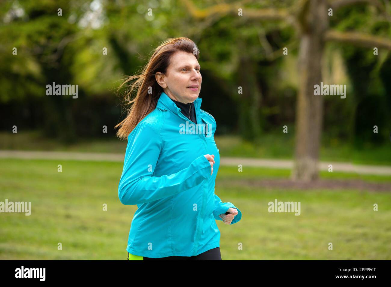 Reife Läuferin, die in einem grünen Park läuft. Rothaarige weiße Dame, in Sportkleidung, hält sich fit, indem sie in der Natur läuft. Stockfoto