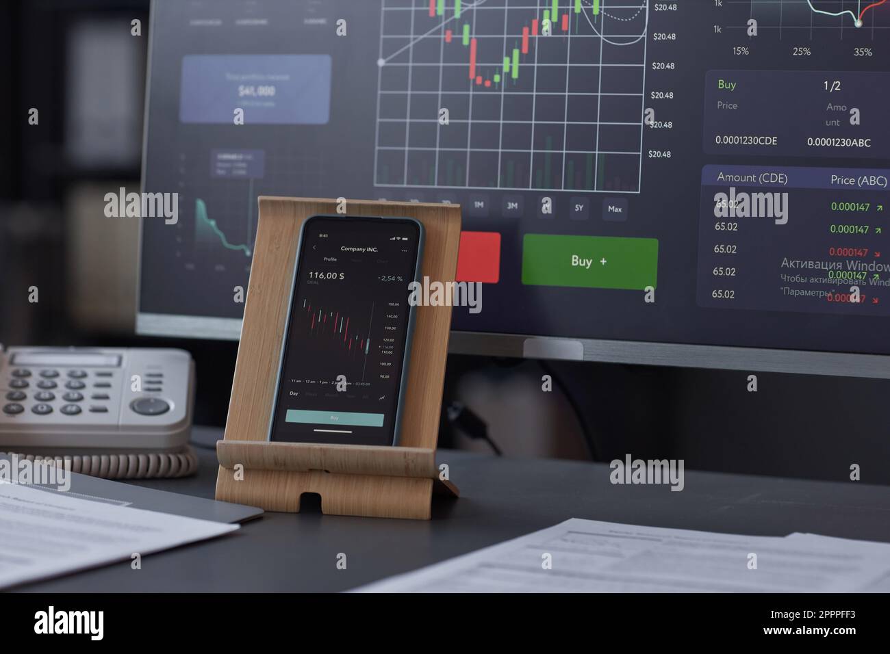 Nahaufnahme eines Smartphones mit Finanzdiagrammen auf dem Bildschirm, der auf einem Tisch steht und Computer im Büro hat Stockfoto
