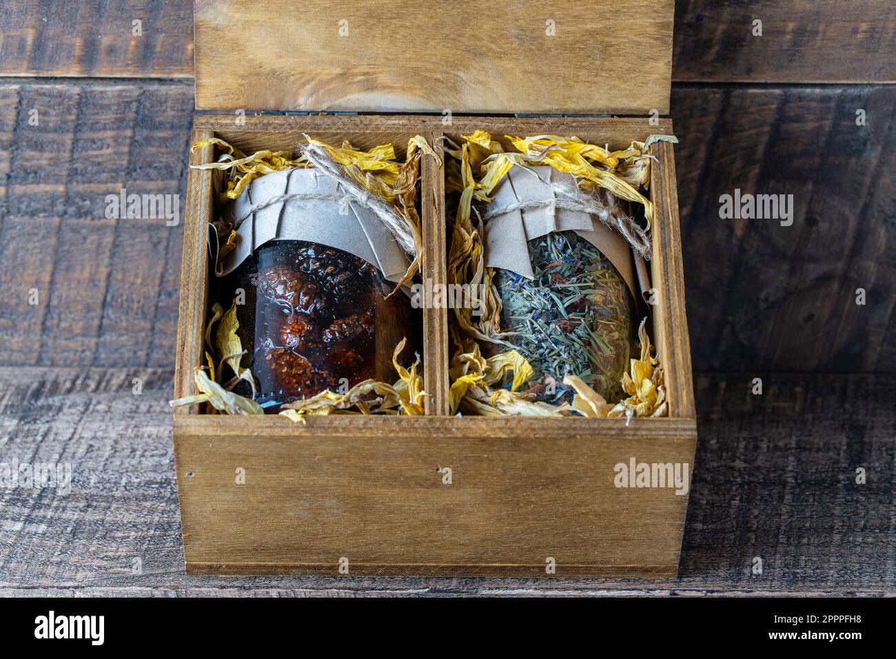 Glasbecher mit Blumentee und Glasbecher mit Kiefernkonfitüre in einer hölzernen Geschenkbox auf einem Tisch, Nahaufnahme. Schönes Geschenk für Familie und Freunde Stockfoto
