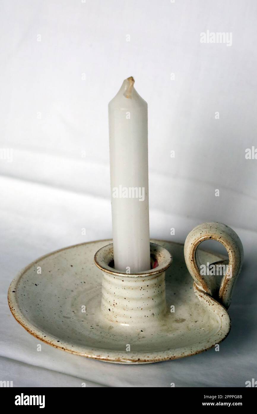 Einfache weiße, unbeleuchtete Kerze in einem Kerzenhalter für Töpferwaren auf weißem Hintergrund Stockfoto