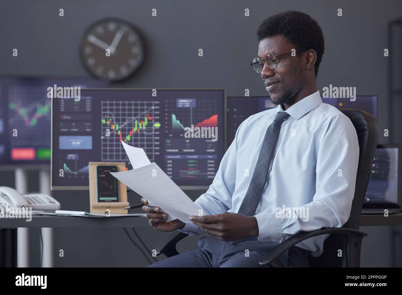 Afroamerikanischer Händler, der Finanzdokumente prüft, während er an seinem Arbeitsplatz im Büro sitzt Stockfoto