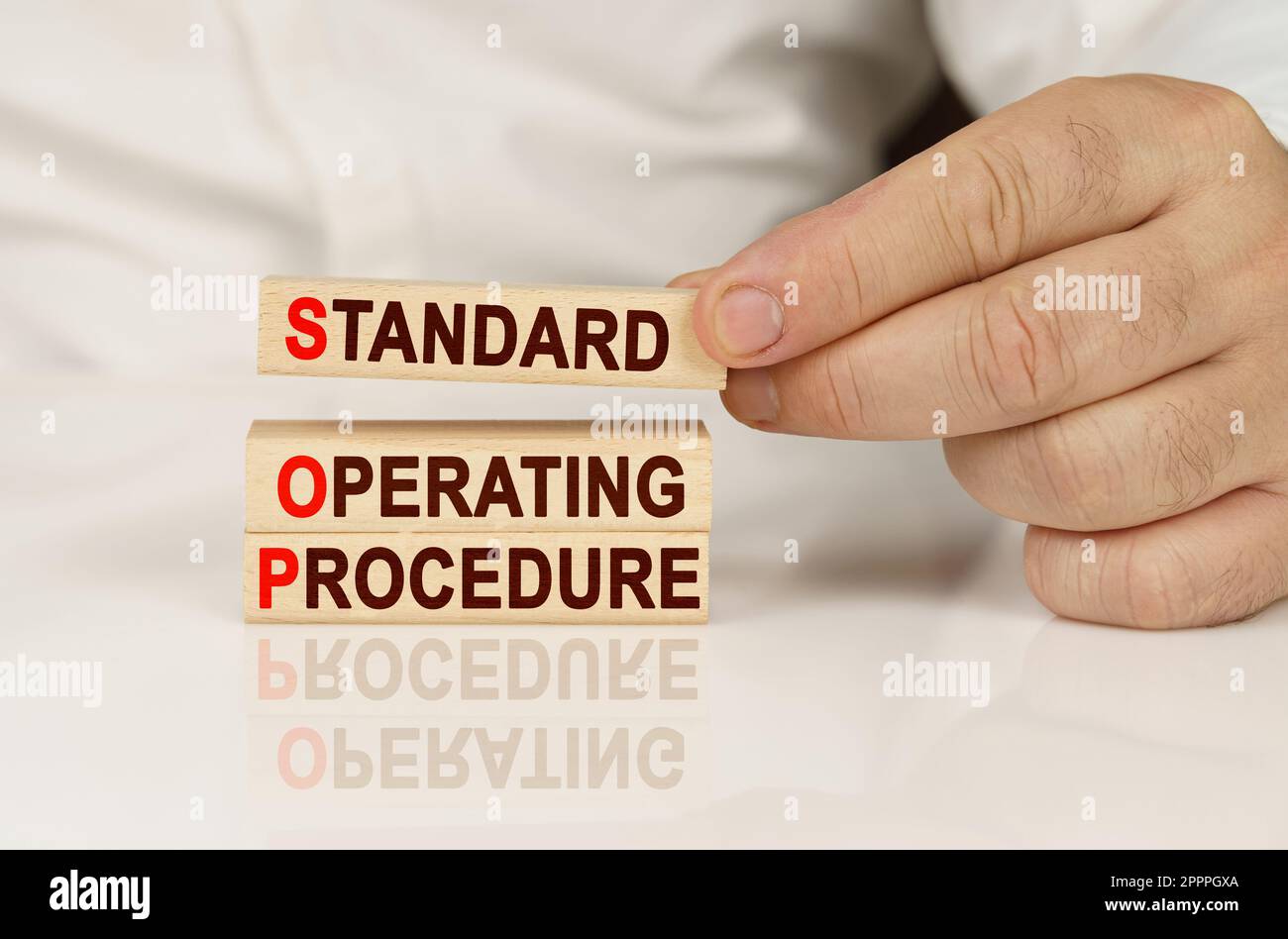 Geschäftskonzept. In den Händen einer Person und auf einer reflektierenden Oberfläche befinden sich Holzblöcke mit der Aufschrift - Standard Operating Procedure Stockfoto