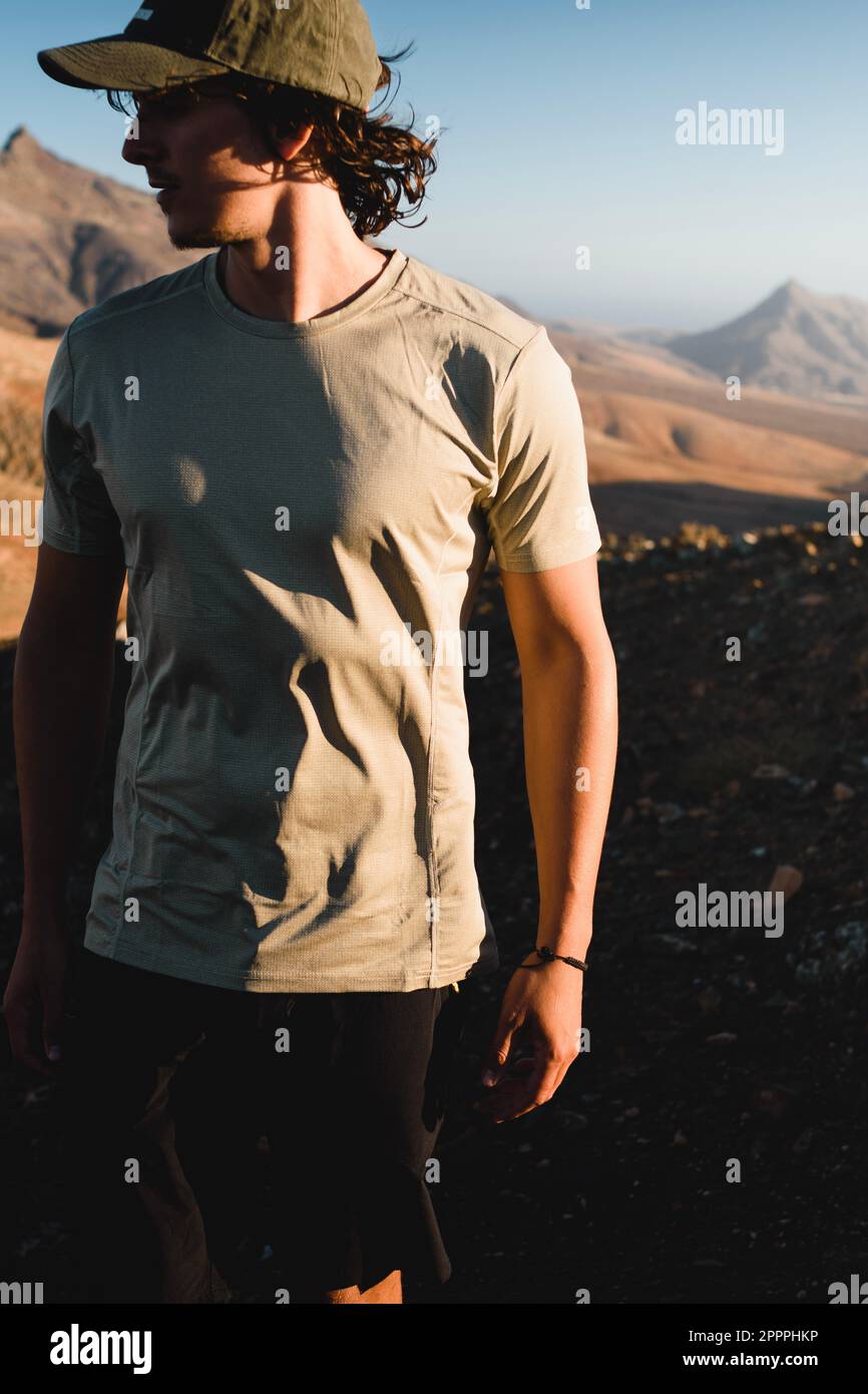 Porträt eines abenteuerlustigen jungen Mannes bei Sonnenuntergang in einer Wüstenlandschaft der Berge von Fuerteventura auf den kanarischen Inseln während einer Wanderung Stockfoto