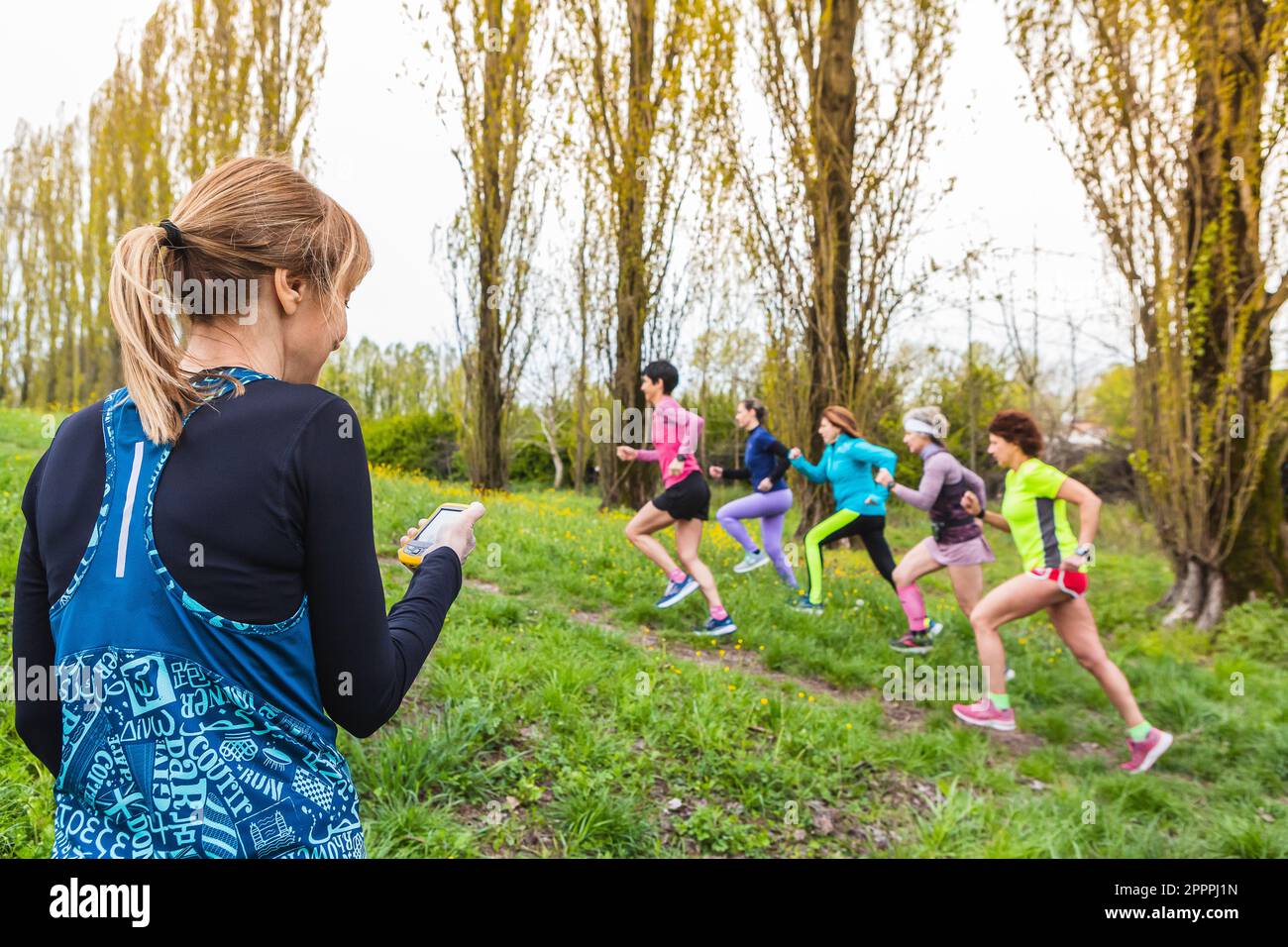 Trainer, der eine Gruppe von Läuferinnen im Freien trainiert, indem er sie bergauf laufen lässt. Stoppuhr in der Hand, Sportbekleidung und professionelle Luft Stockfoto