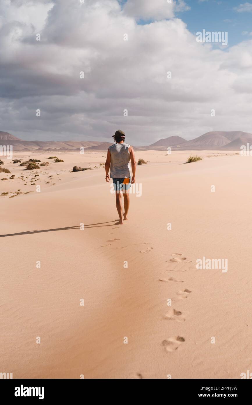 Junger Mann, der im Sommer auf dem Wüstensand der Dünen von Corralejo in Fuerteventura während einer Urlaubsreise durch die Kanarischen Inseln ruhig spaziert Stockfoto