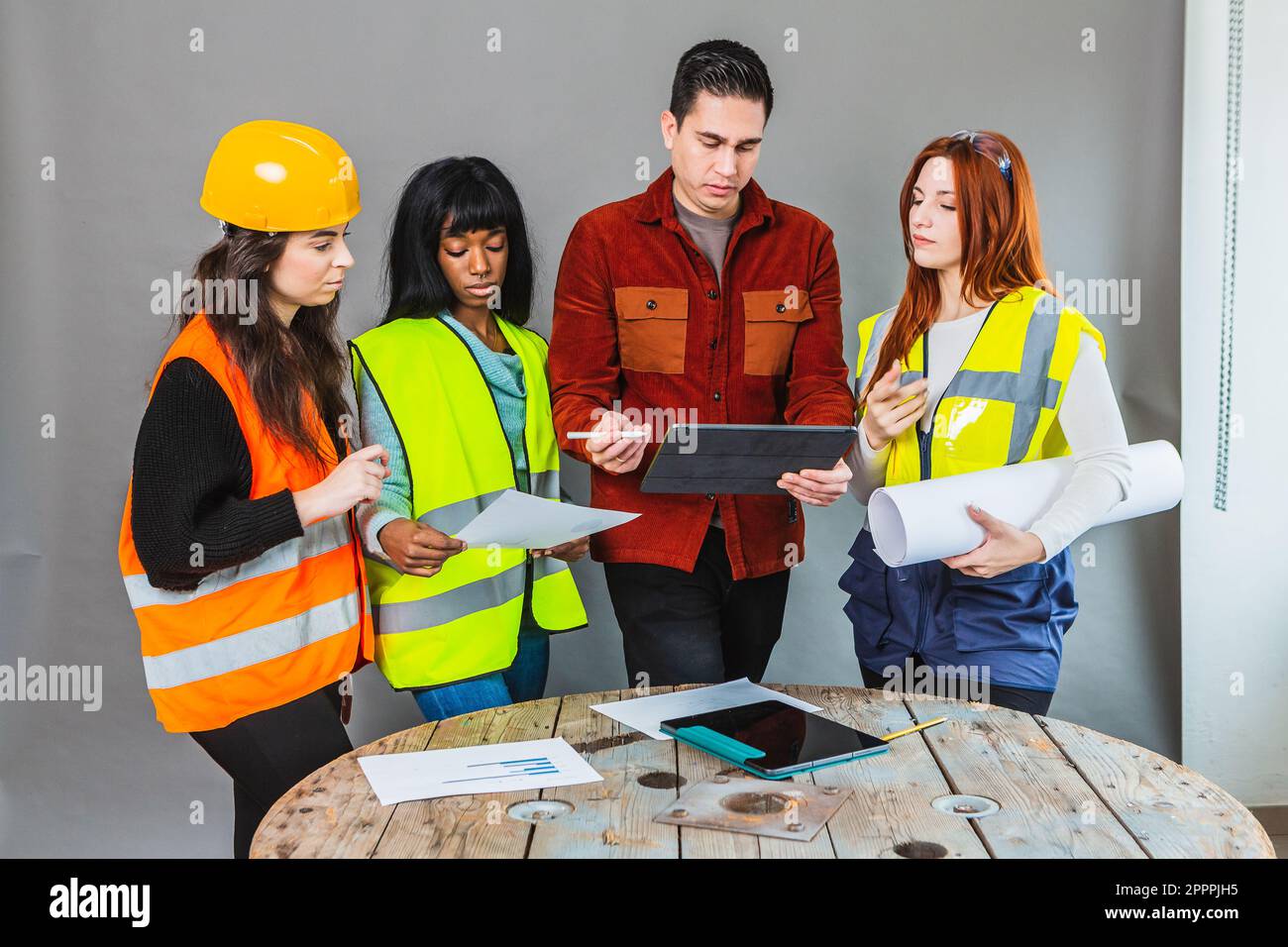 Arbeiterinnen auf einer Baustelle, die mit dem Manager konfrontiert werden. Projekte in der Hand und Tablet mit Informationen. Gehirnstürme vor der Arbeit Stockfoto