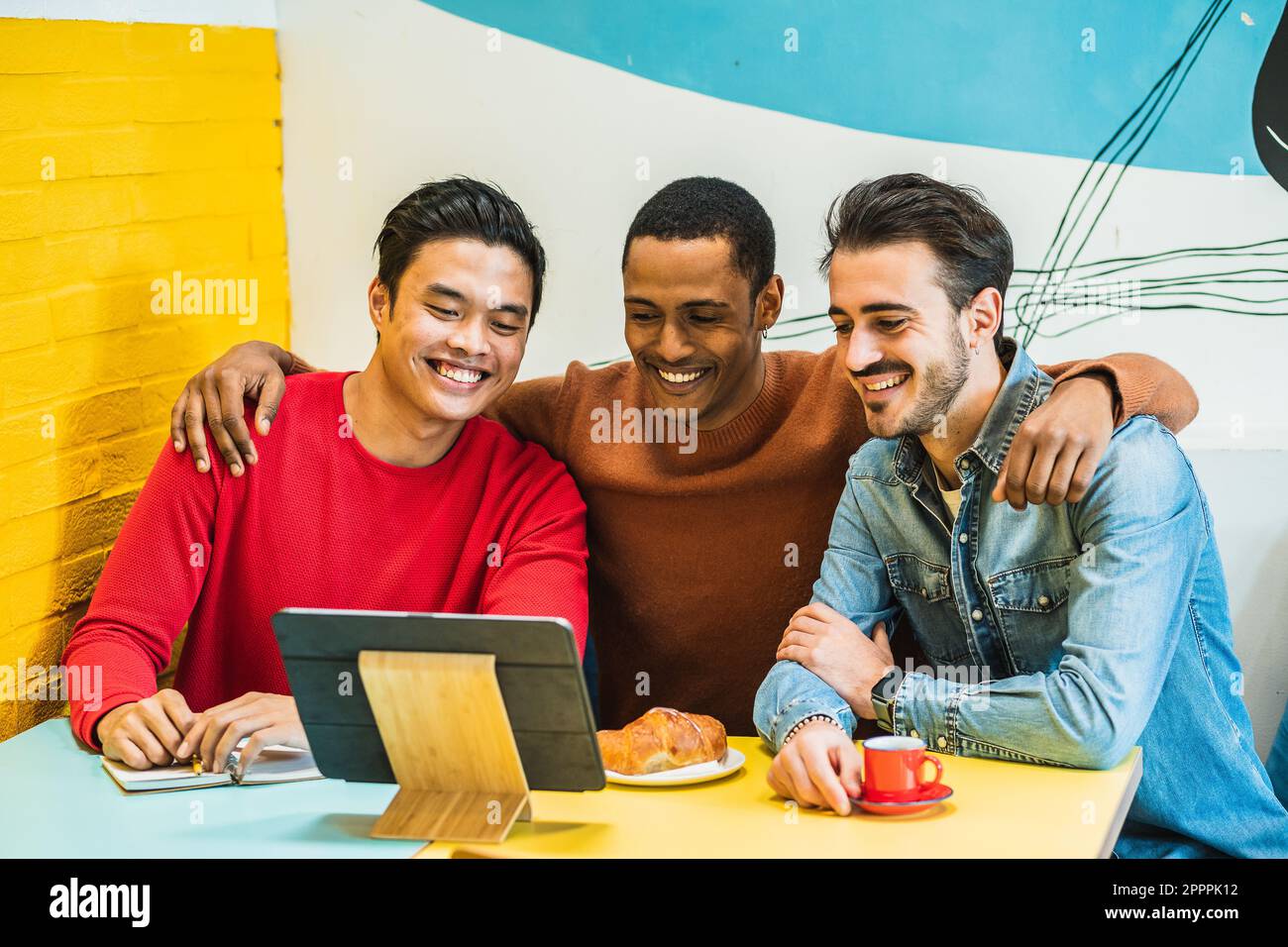 Freunde, die während des Frühstücks an einem Tisch in einem Café sitzen und sich ein lustiges Video auf ihrem Tablet anschauen. Ein Moment des Spaßes und der Entspannung. Stockfoto