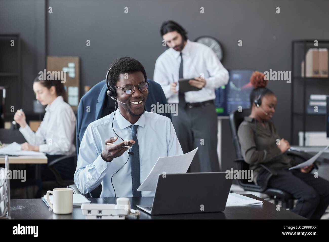 Afroamerikanischer Makler für Kopfhörer, der mit Kunden spricht, während er mit einem Laptop an seinem Arbeitsplatz sitzt Stockfoto
