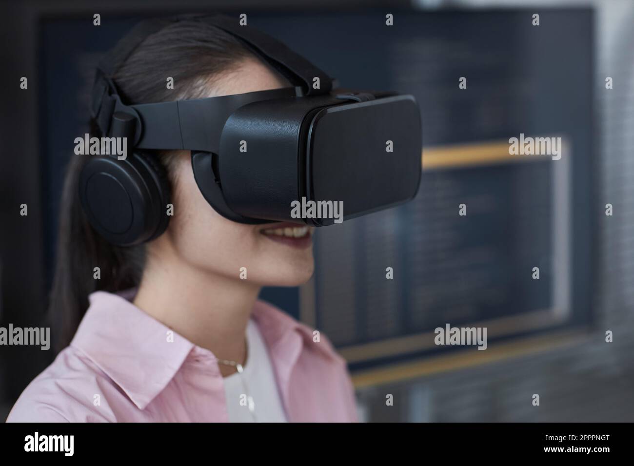 Junge lächelnde Frau mit VR-Brille, die während des Virtual-Reality-Spiels ein neues Computerprogramm testet Stockfoto