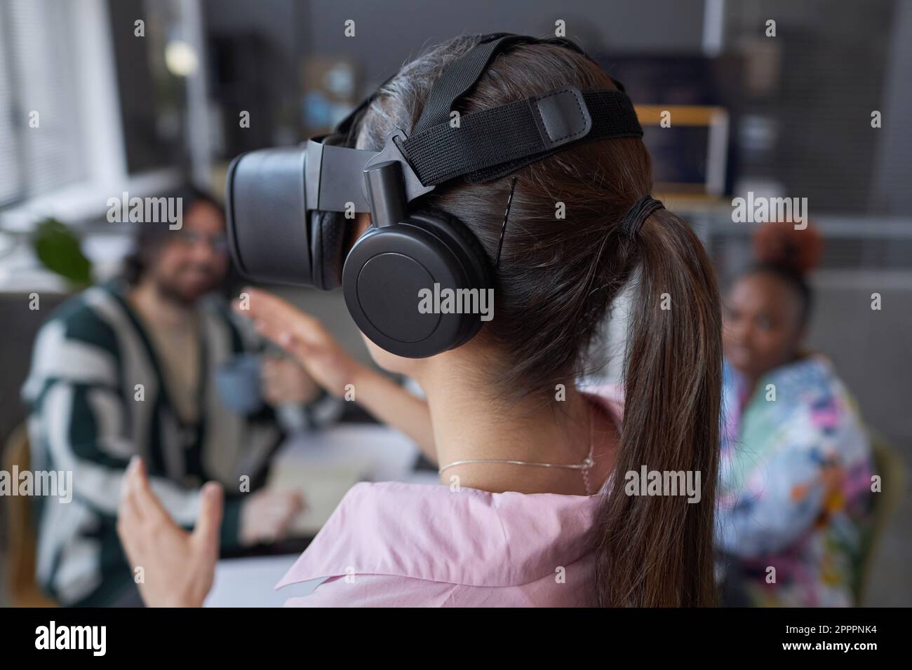 Rückansicht einer jungen Frau, die zusammen mit ihren Kollegen während der Teamarbeit bei einem Meeting eine VR-Brille testet Stockfoto