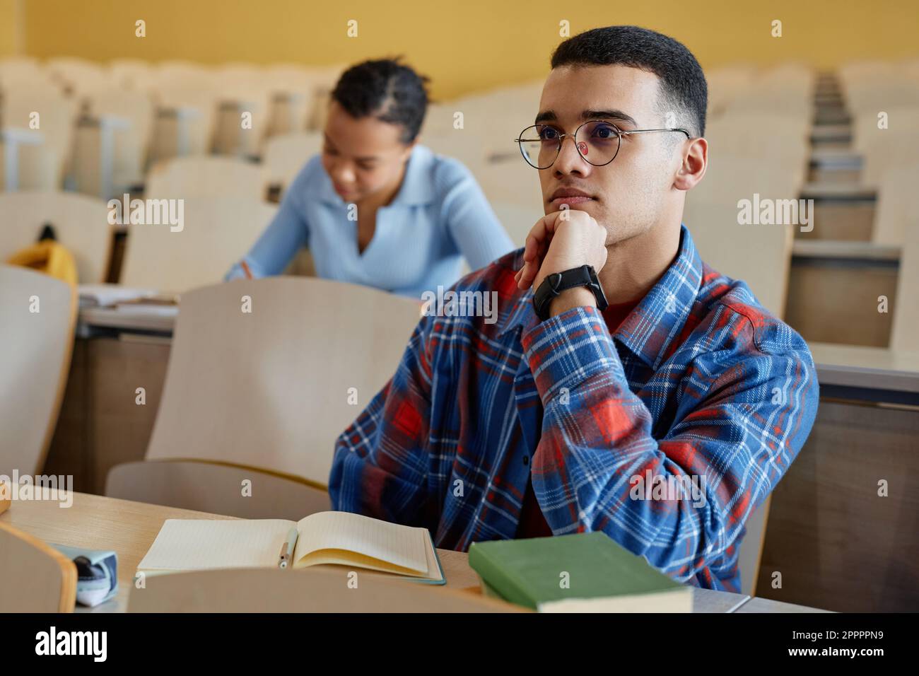 Teenager mit Brille, sitzt am Schreibtisch und hört während des Vortrags an der Universität einem Dozenten zu Stockfoto