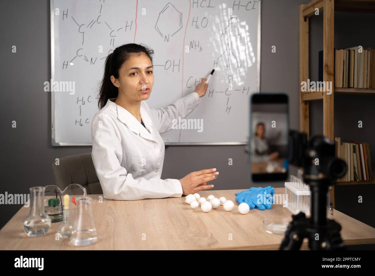 Eine Lehrerin, die einen Videovortrag hält und Chemie online lehrt und auf eine Tafel zeigt, mit Formeln zu Hause. E-Unterricht und Bloggen im Bildungsbereich Stockfoto