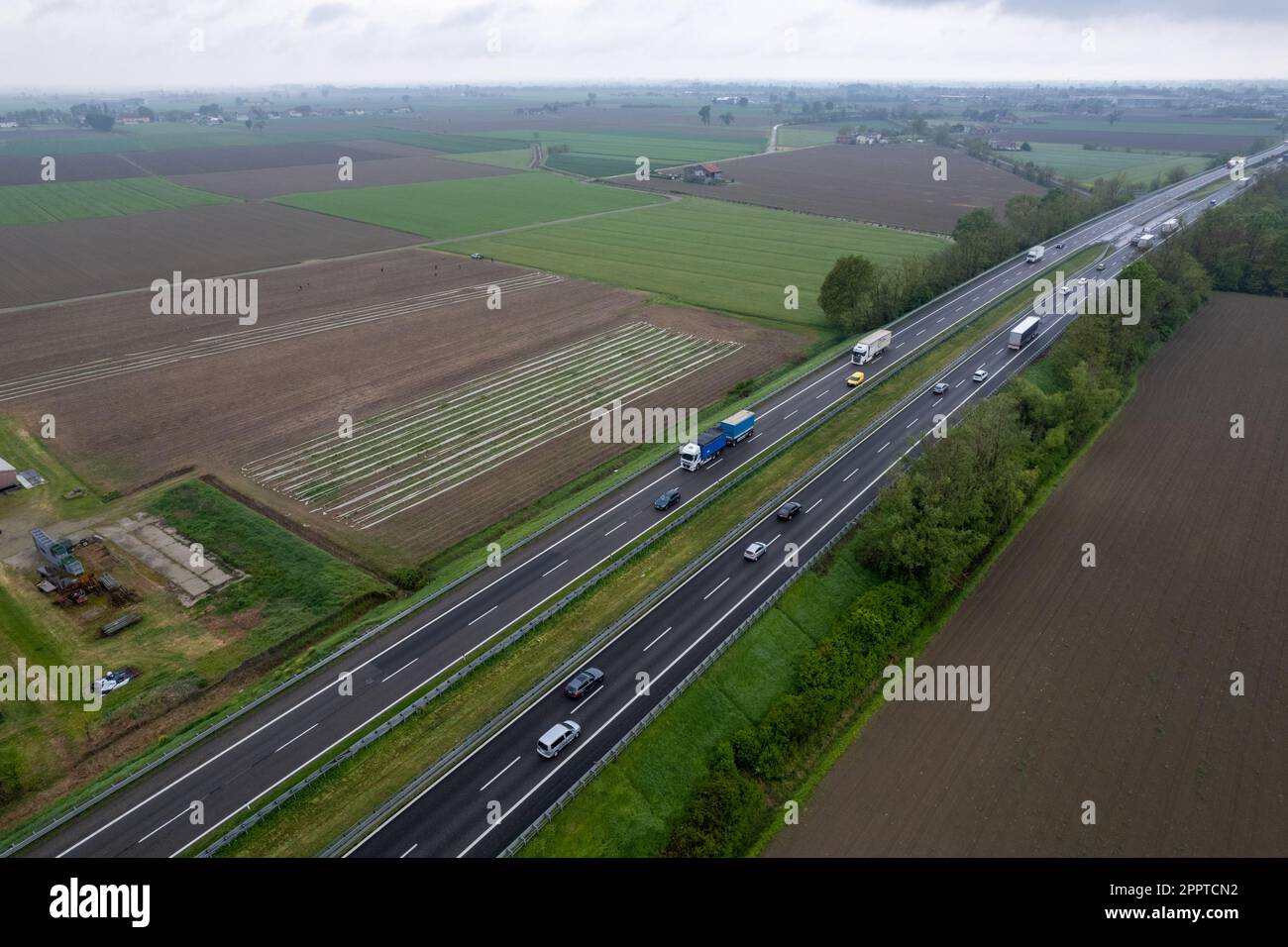 Piacenza, Italien - April 2023 Cargo LKWs und Pkw auf der Autobahn A1 Autostrada del Sone aus der Vogelperspektive zwischen padainflachen ländlichen Feldern Stockfoto