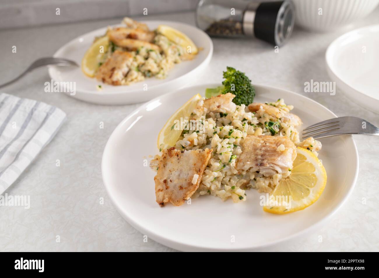 Fitness-Mahlzeit mit gebratenem Fisch in der Pfanne, braunem Reis, Brokkoli und Schalotten auf einem Teller Stockfoto