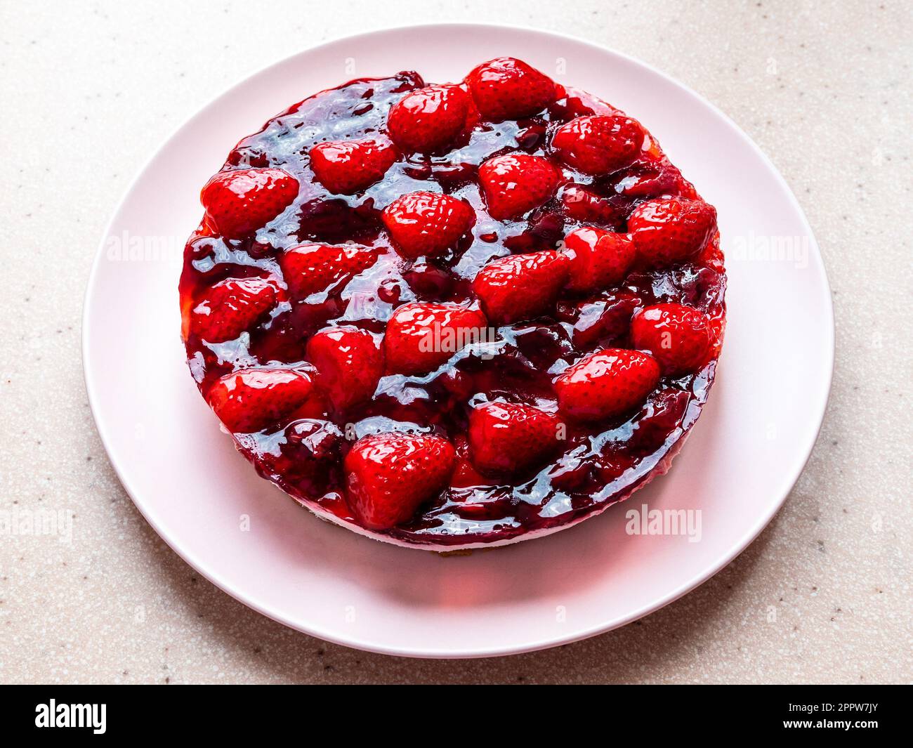 Süßer Kuchen mit Erdbeeren und Kirschen auf rosafarbenem Teller und rosafarbenem Steinbrett Stockfoto