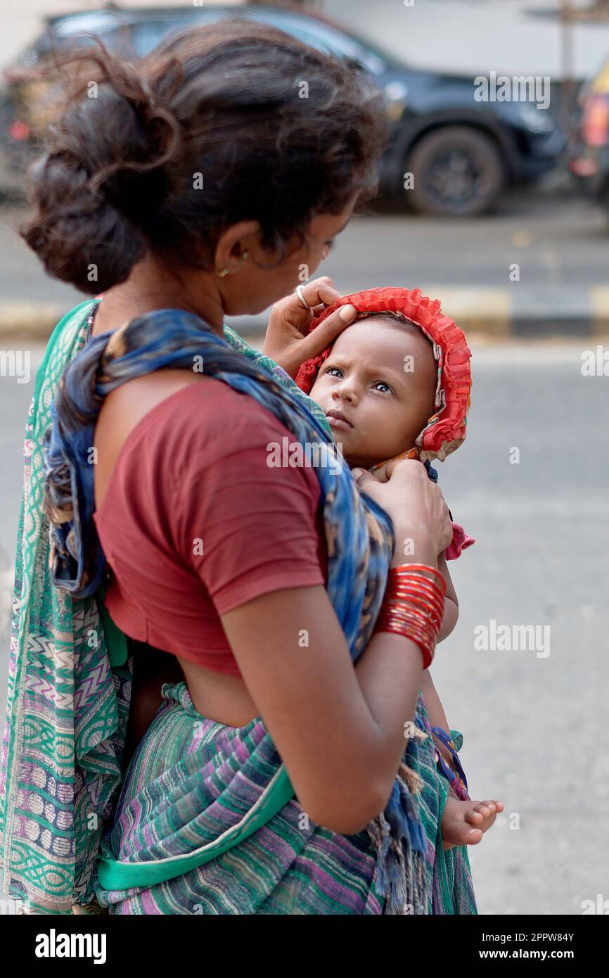 Eine junge Bettler-Frau in Mumbai, Indien, trägt ihren kleinen Jungen, der sie mit unkindlicher Intensität oder Ernsthaftigkeit ansieht Stockfoto