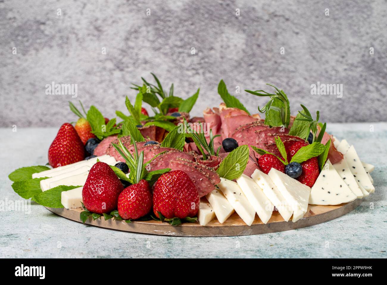 Antipasto-Set-Teller. Kaltgeräucherter Fleischteller. Antipasto mit Schinken, Prosciutto, Salami, Blauschimmelkäse, Mozzarella mit Blaubeeren und Erdbeeren Stockfoto
