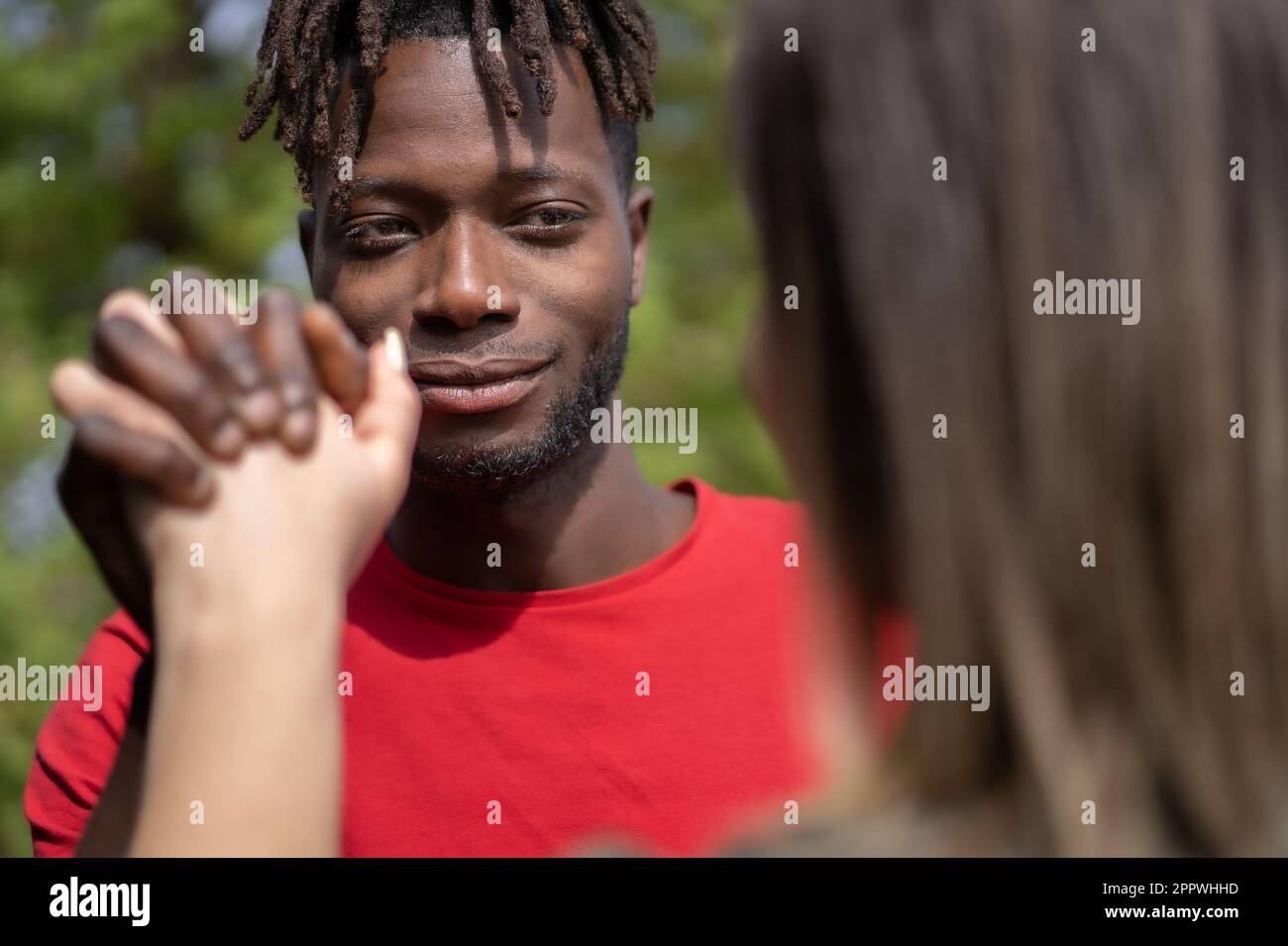 Nahaufnahme der verflochtenen schwarzen und weißen Hände eines jungen gemischtrassigen Paares, Männergesicht sichtbar mit lockigem Haar und Dreadlocks. Stockfoto