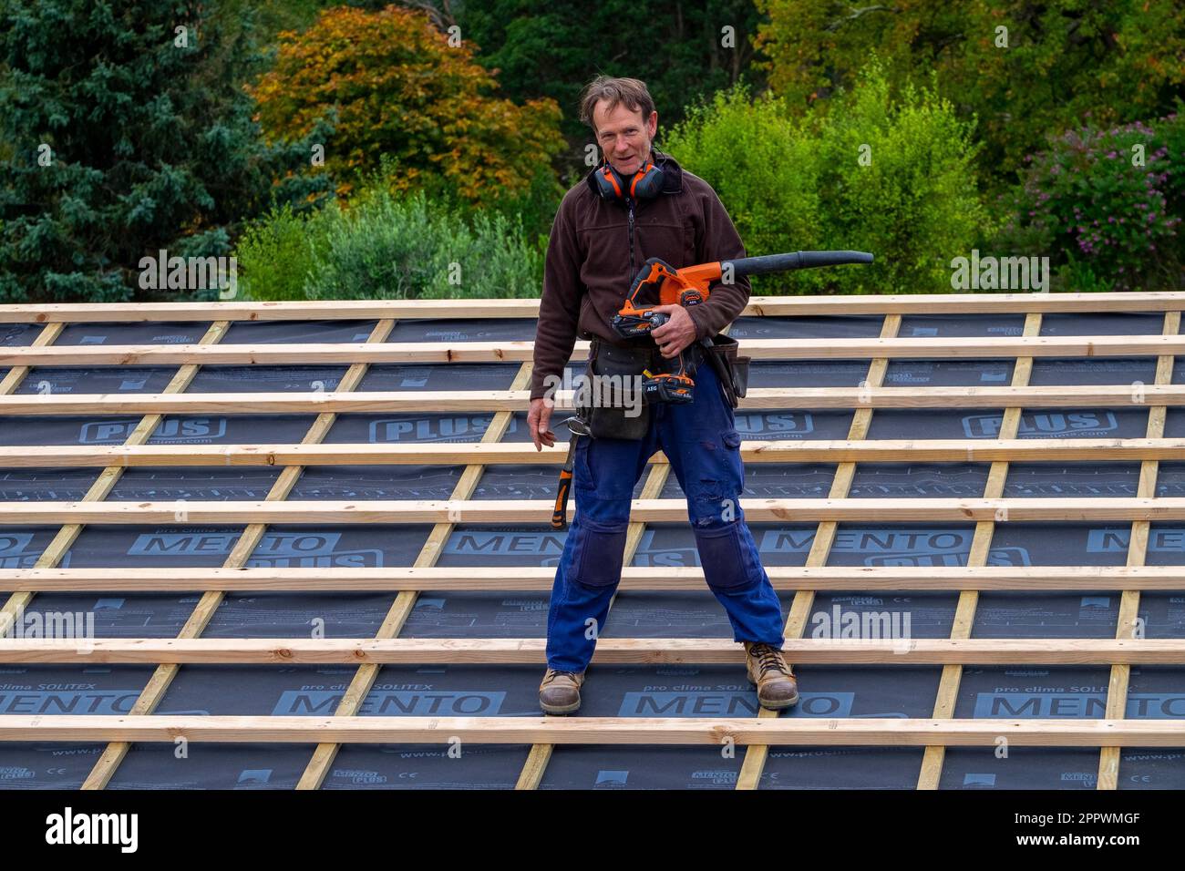 Arbeiter steht auf dem Dach, nachdem er sich über der Isolierung des zu renovierenden Hauses versammelt hat Stockfoto