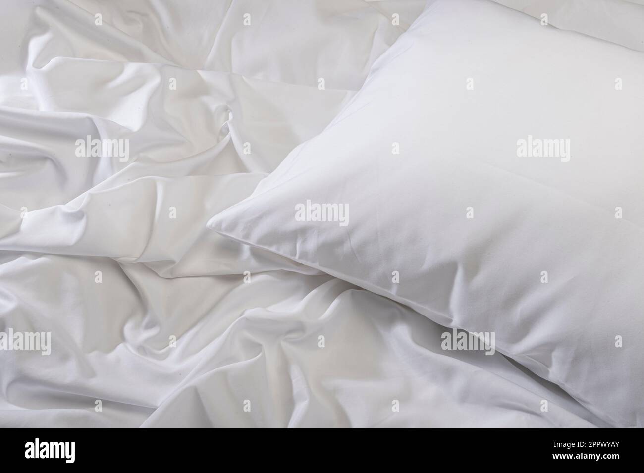 Weißes Kissen auf dem Bett mit zerknitterten Laken Stockfoto