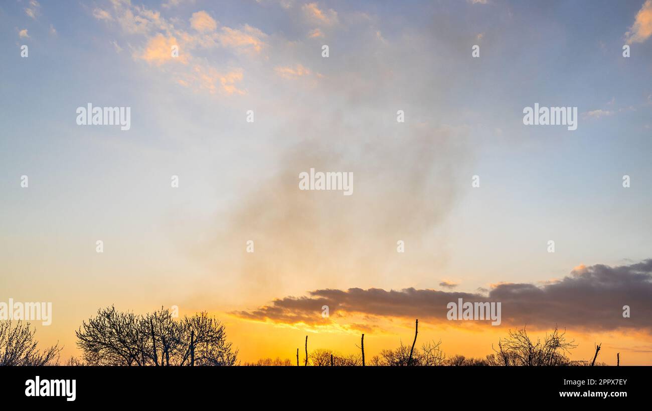 Panoramablick auf den Sonnenuntergang am Himmel mit Rauch vom Lagerfeuer am Frühlingsabend Stockfoto