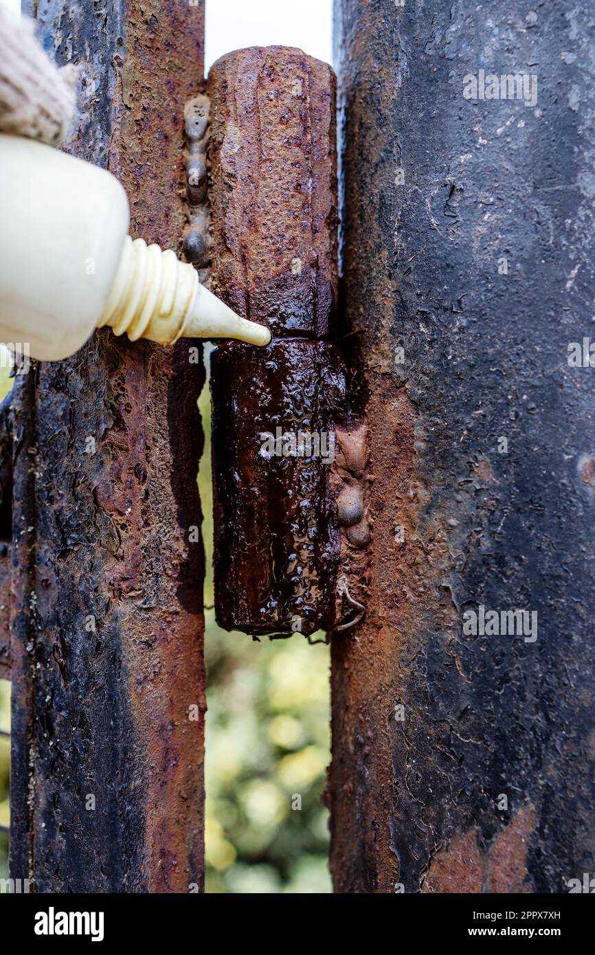 Das alte Torscharnier schmiert mit Öl aus der Schließung des Kunststoffölers im Freien Stockfoto