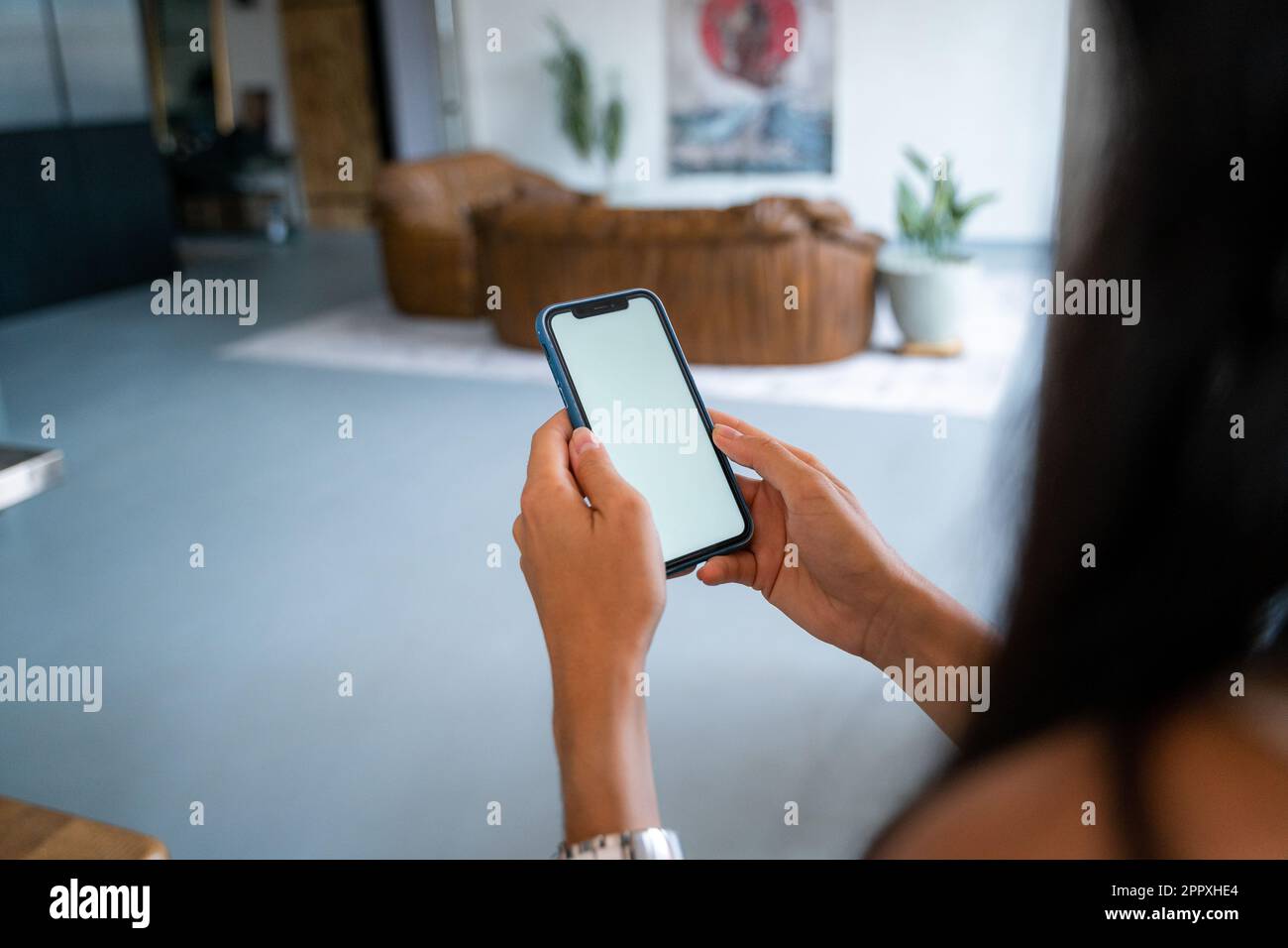 Von oben gekürzt, unwiedererkennbare junge Frau in lässiger Kleidung, sitzt auf dem Sofa und surft im Smartphone, während sie sich in einem gemütlichen Wohnzimmer zu Hause ausruht und Stockfoto