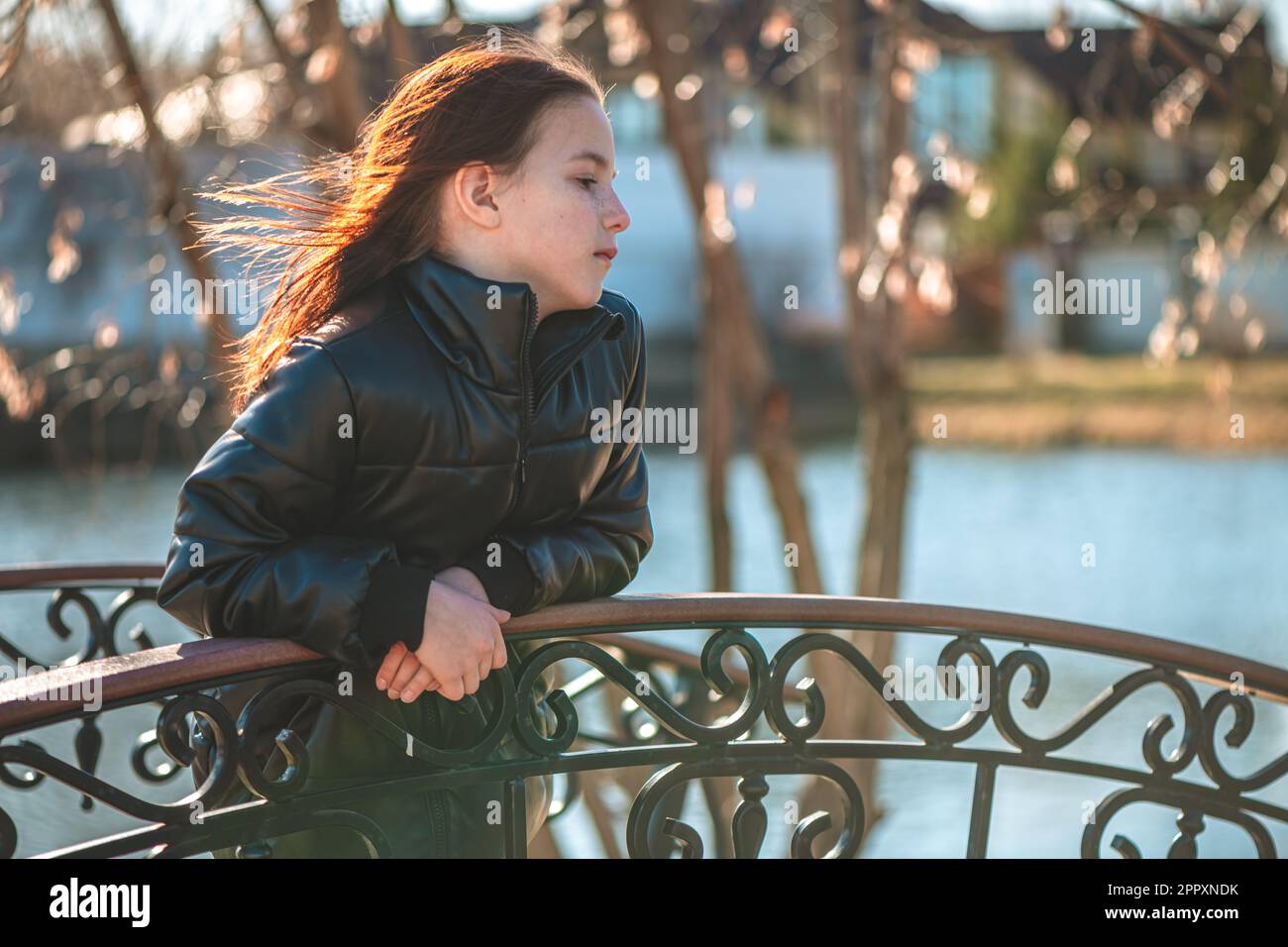 Ein pensives Mädchen im Schulalter steht auf der Brücke und schaut in die Ferne Stockfoto