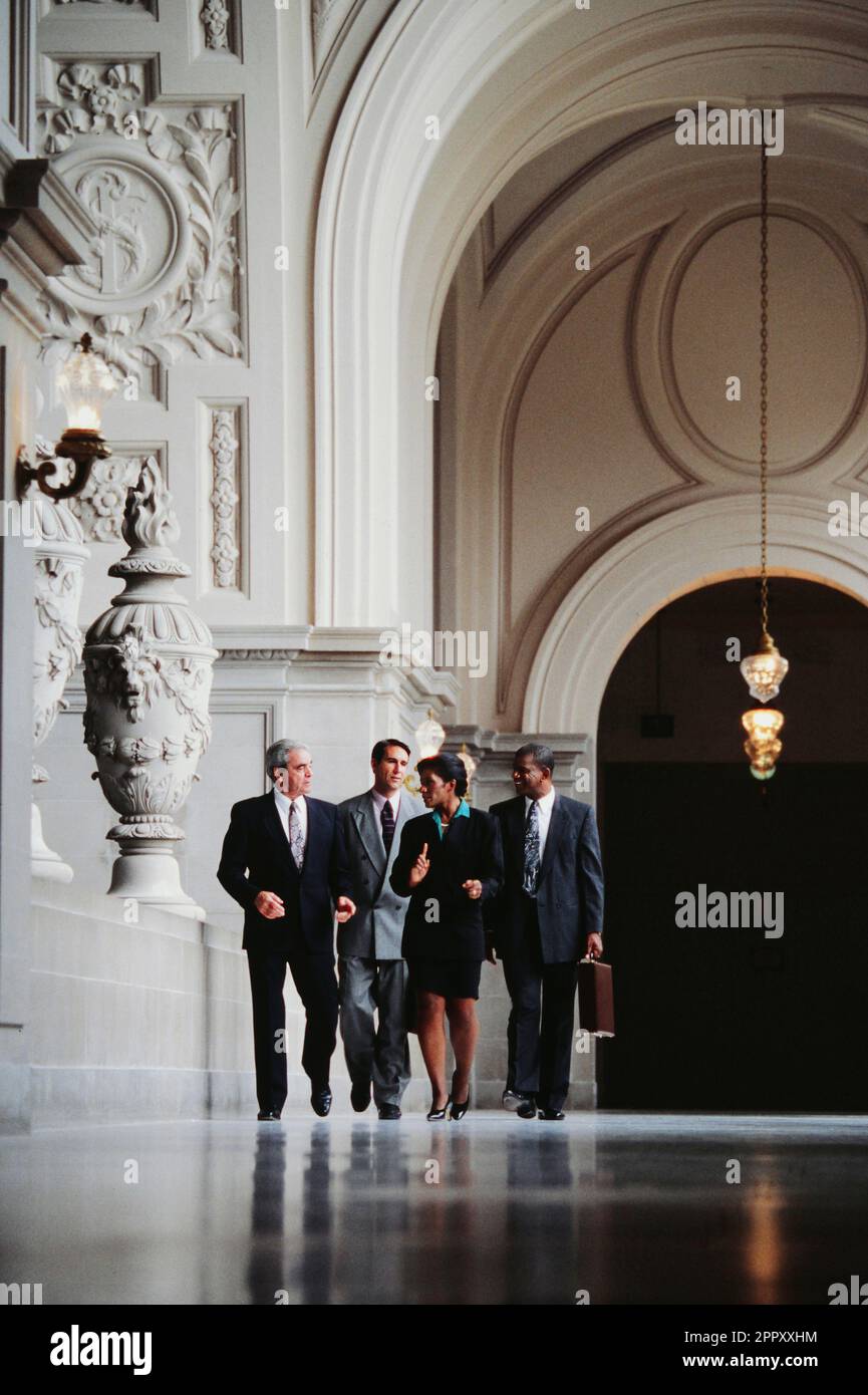 Eine Gruppe entschlossener afroamerikanischer und kaukasischer Führungskräfte, die durch eine kunstvoll verzierte Lobby laufen Stockfoto