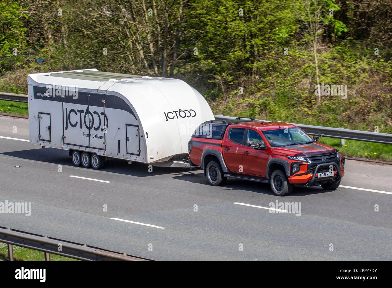 JCT600 Home Delivery 3-achsiger Anhänger wird von 2021 Mitsubishi L200 Barbarian Di-D Auto Di-D 150 INVECS-II Sports Mode Auto Start/Stop Orange LCV Double Cab Pick Up Diesel 2268 cm3 gezogen; Fahrt auf der Autobahn M61, Großbritannien Stockfoto