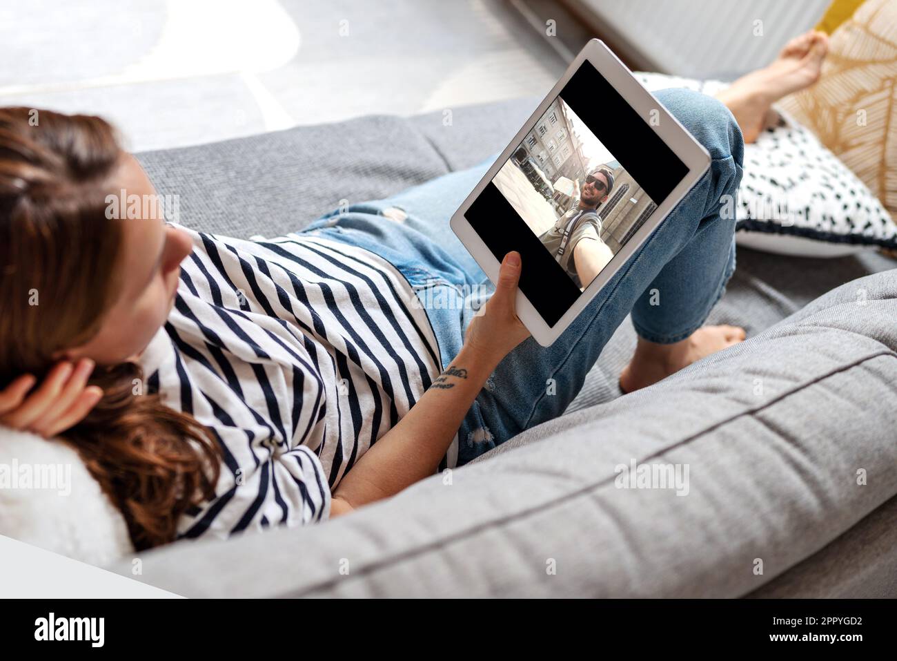 Frau, die zu Hause auf dem Sofa liegt und sich mit ihrem digitalen Tablet und dem Internet ein Video-Blog ansieht. Stockfoto