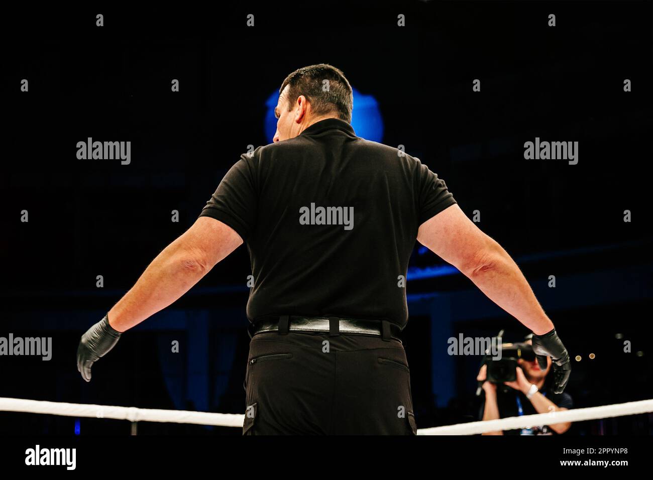 Rückansicht des Schiedsrichters, der während eines MMA-Kampfes im Ring steht, auf dunklem Hintergrund Stockfoto