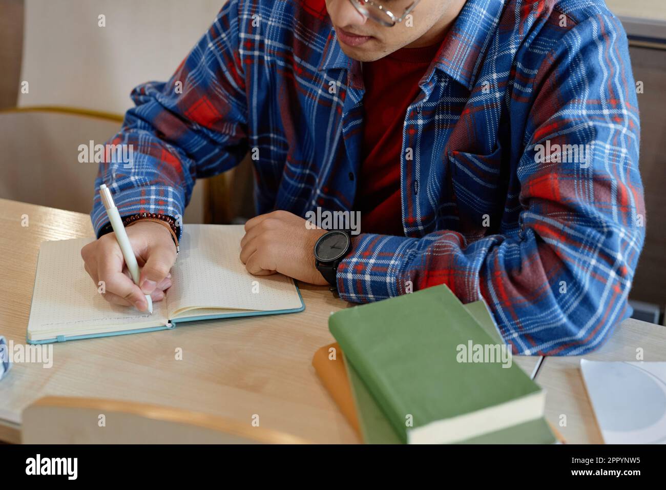 Aus einem großen Blickwinkel kann der Schüler Notizen in seinem Notizbuch machen, während er während des Vortrags am Schreibtisch sitzt Stockfoto