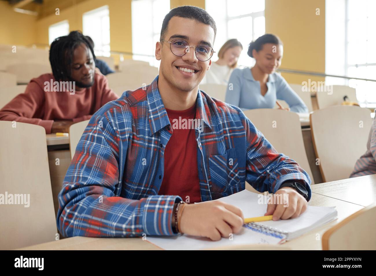 Porträt eines Schülers mit Brille, der vor der Kamera lächelt, während er beim Vortrag am Schreibtisch sitzt Stockfoto