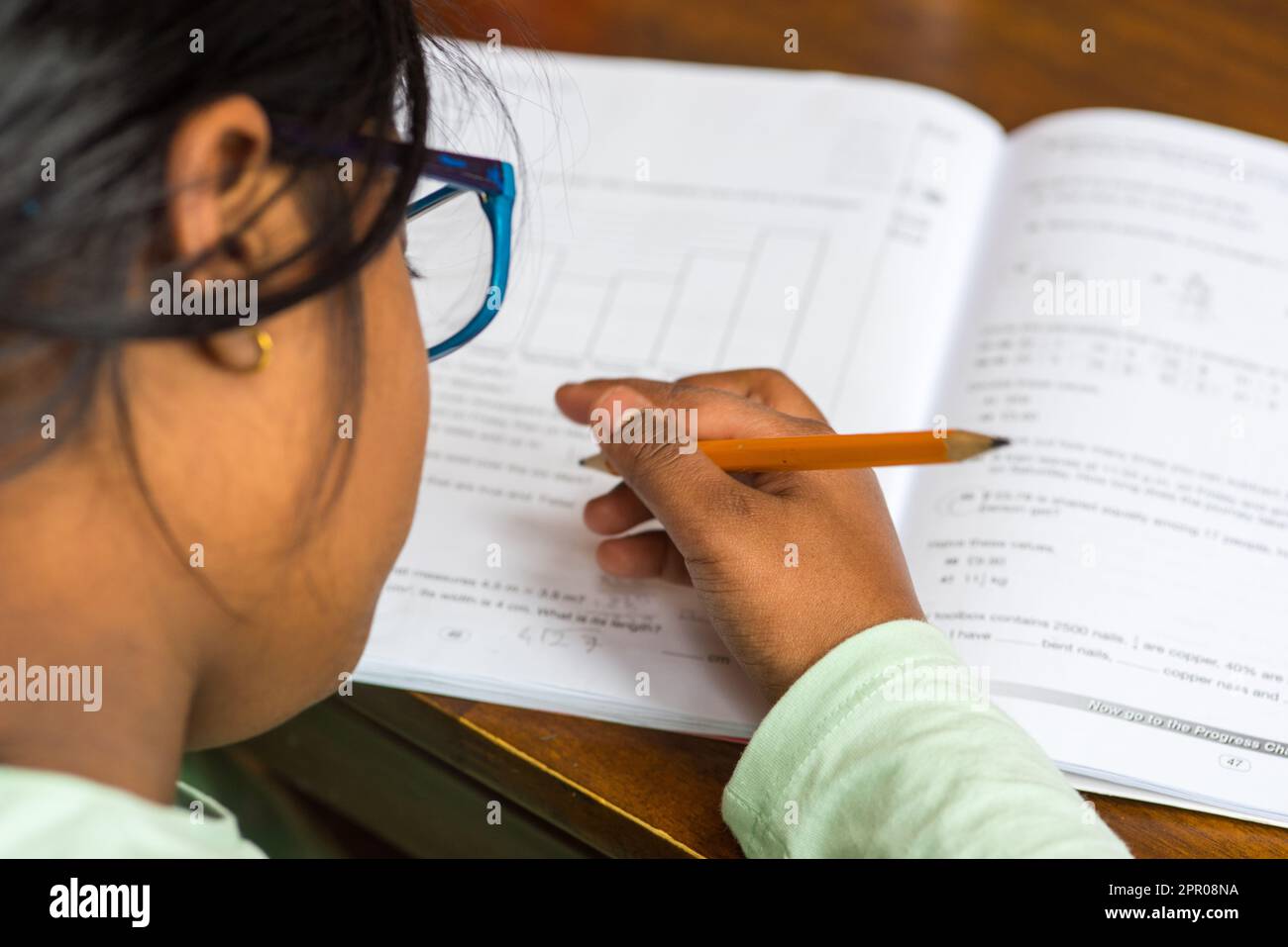 Ein Mädchen im Alter von 9 Jahren schreibt mit einem Bleistift auf ein Buch Stockfoto