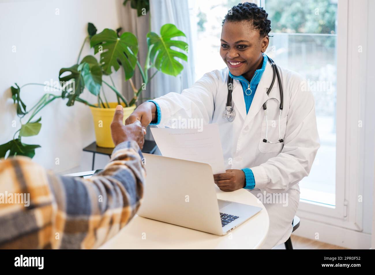 Junge Ärztin schüttelt sich die Hand mit dem Patienten, nachdem sie die Ergebnisse ihrer Untersuchungen vorgelegt hat. Konzept: Medizin, Krankheit, Gesundheitsversorgung Stockfoto