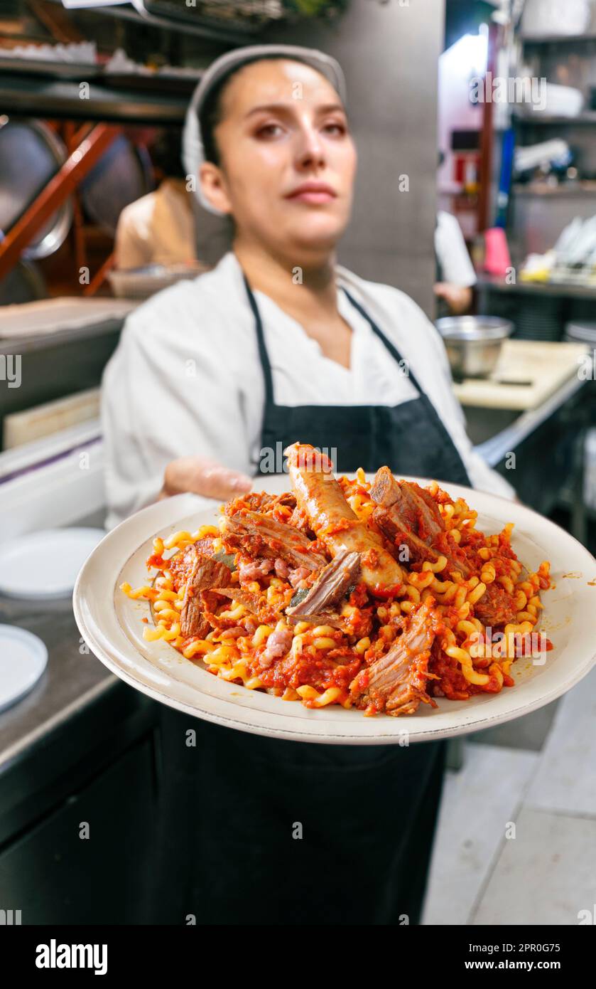 Die weibliche Köchin hält einen Teller ragù Bolognese in einer professionellen Küche, ein traditionelles Nudelgericht mit Fleischsauce aus Italien. Stockfoto
