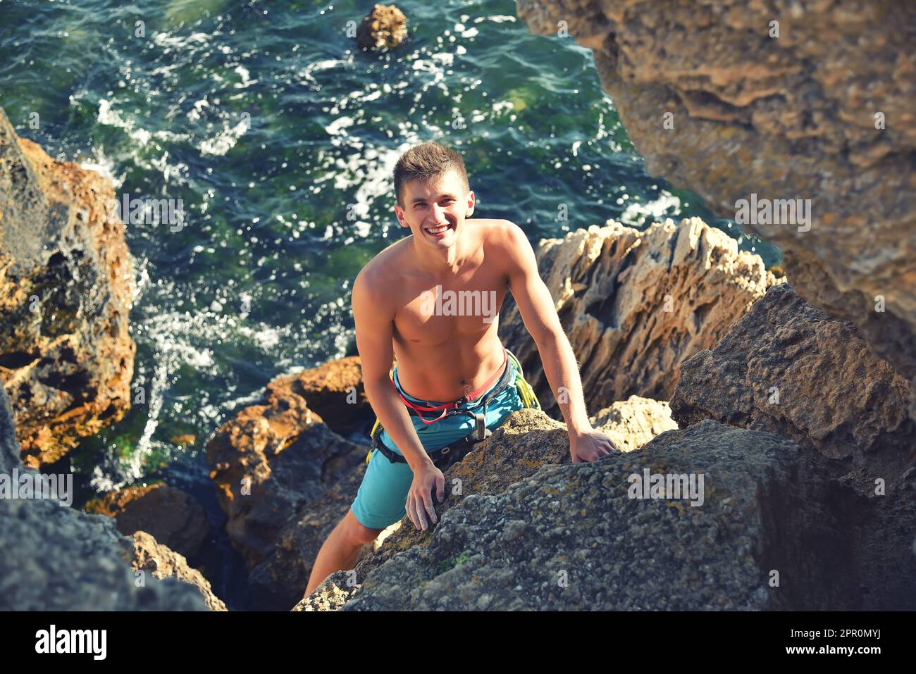 Glücklicher Kletterer, der auf einen Felsen im Meereshintergrund klettert Stockfoto