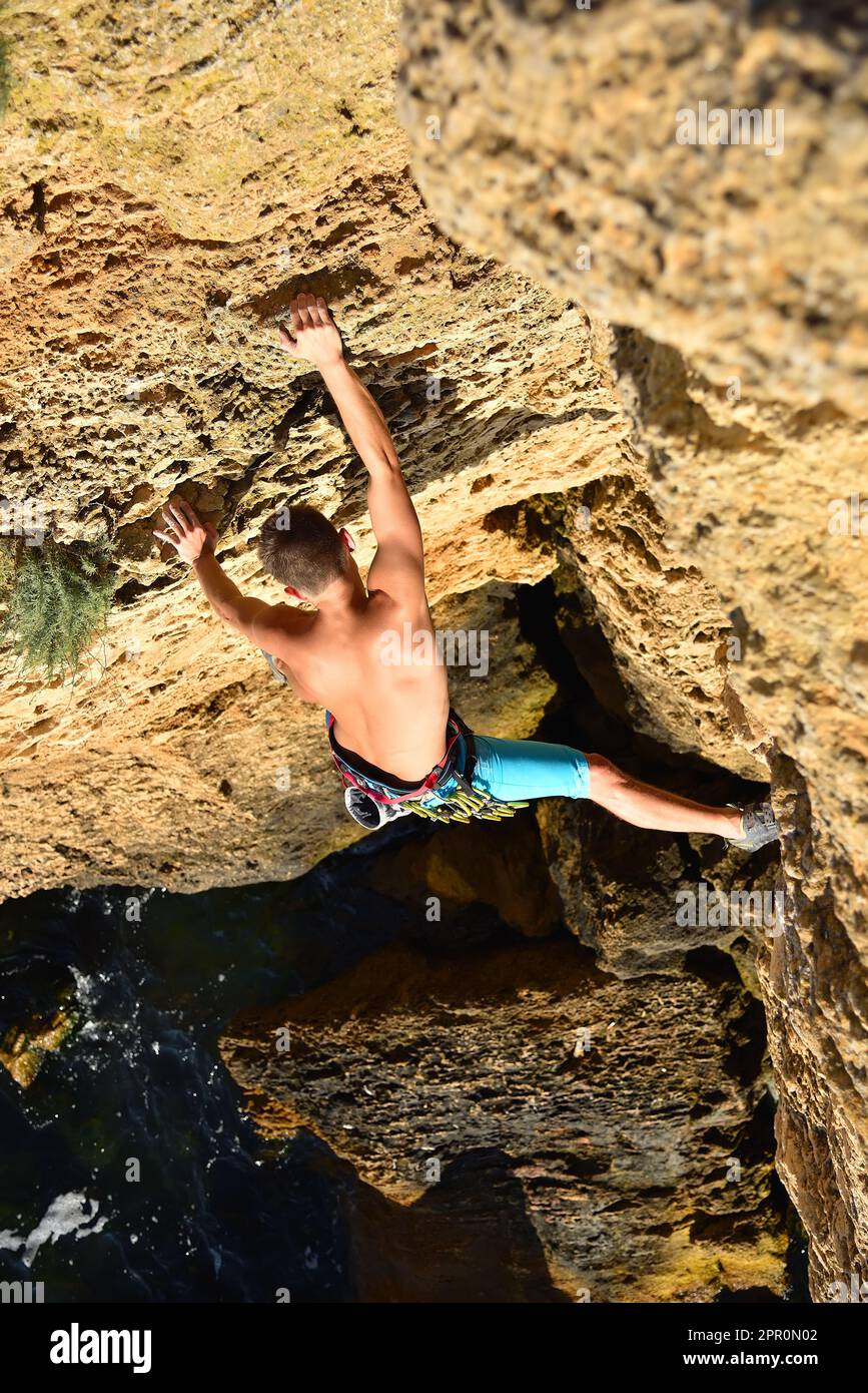 Männlicher Kletterer klettert auf eine Felswand, Blick von oben Stockfoto