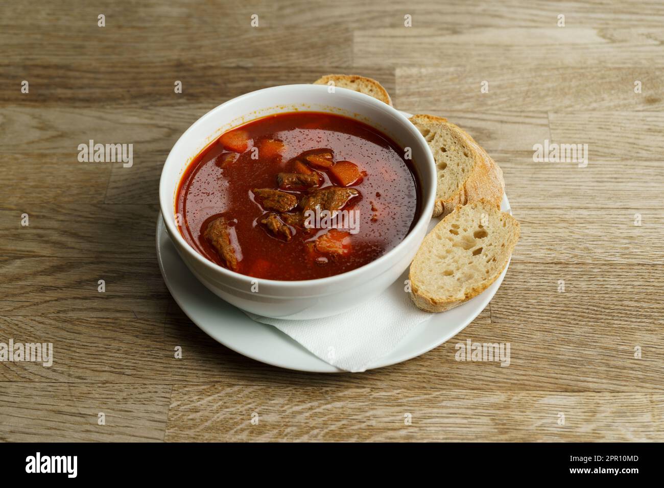 Traditionelle ungarische Gulaschsuppe mit Brot auf einem Holztisch Stockfoto
