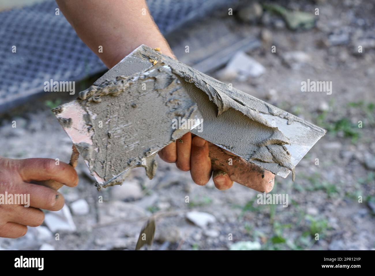 Mann, der die Mischung aus feuchtem Zementmörtel auf eine Maurerkelle mit Metallspritzer auflegt, eine Hand verschwommen, um die Action hervorzuheben, Nahaufnahme Stockfoto