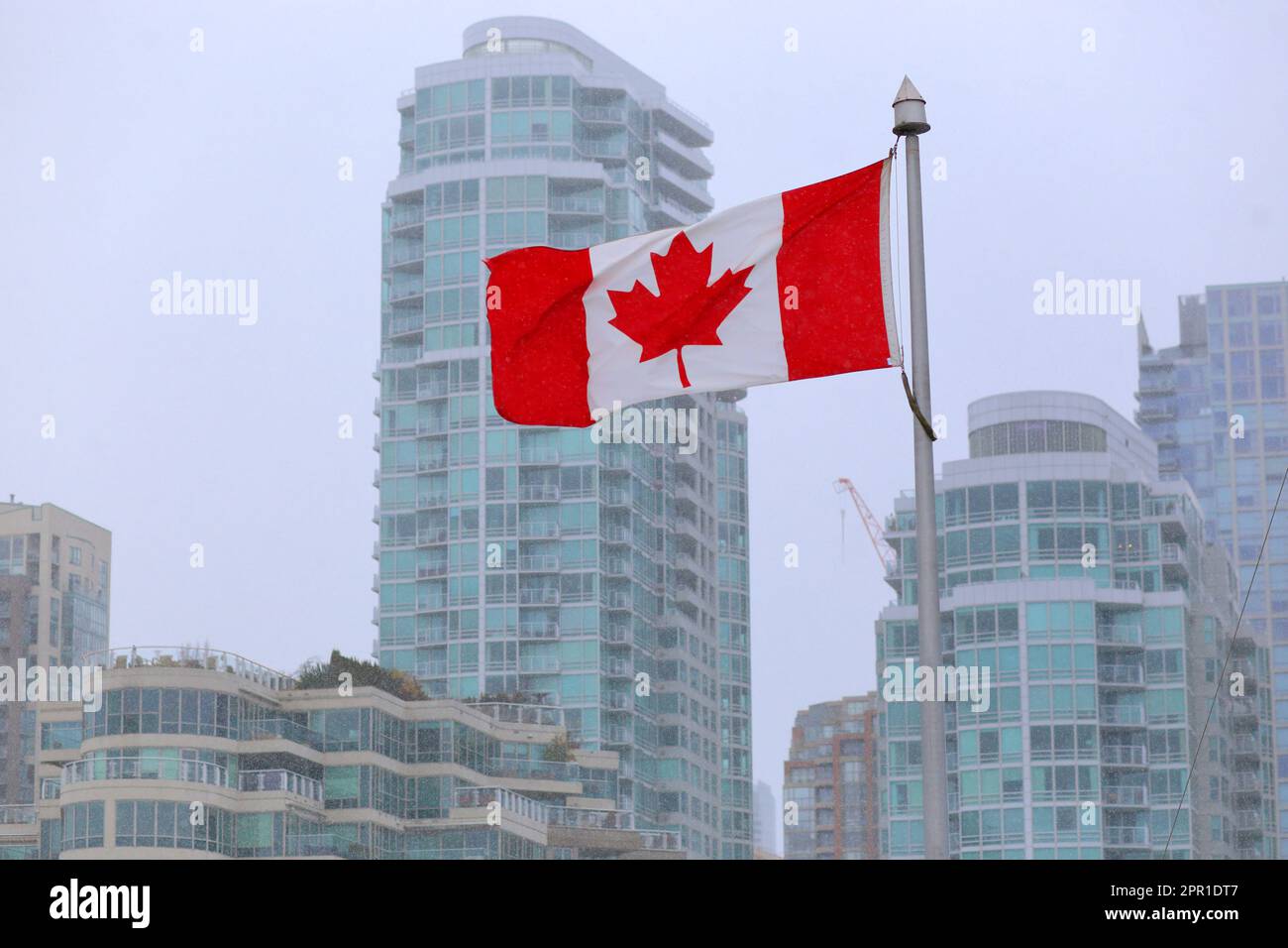 Die kanadische Flagge fliegt an einem schneebedeckten Tag in Vancouver, British Columbia, Kanada, mit Downtown-Uferwohnungen und gentrifizierten Gebäuden Stockfoto