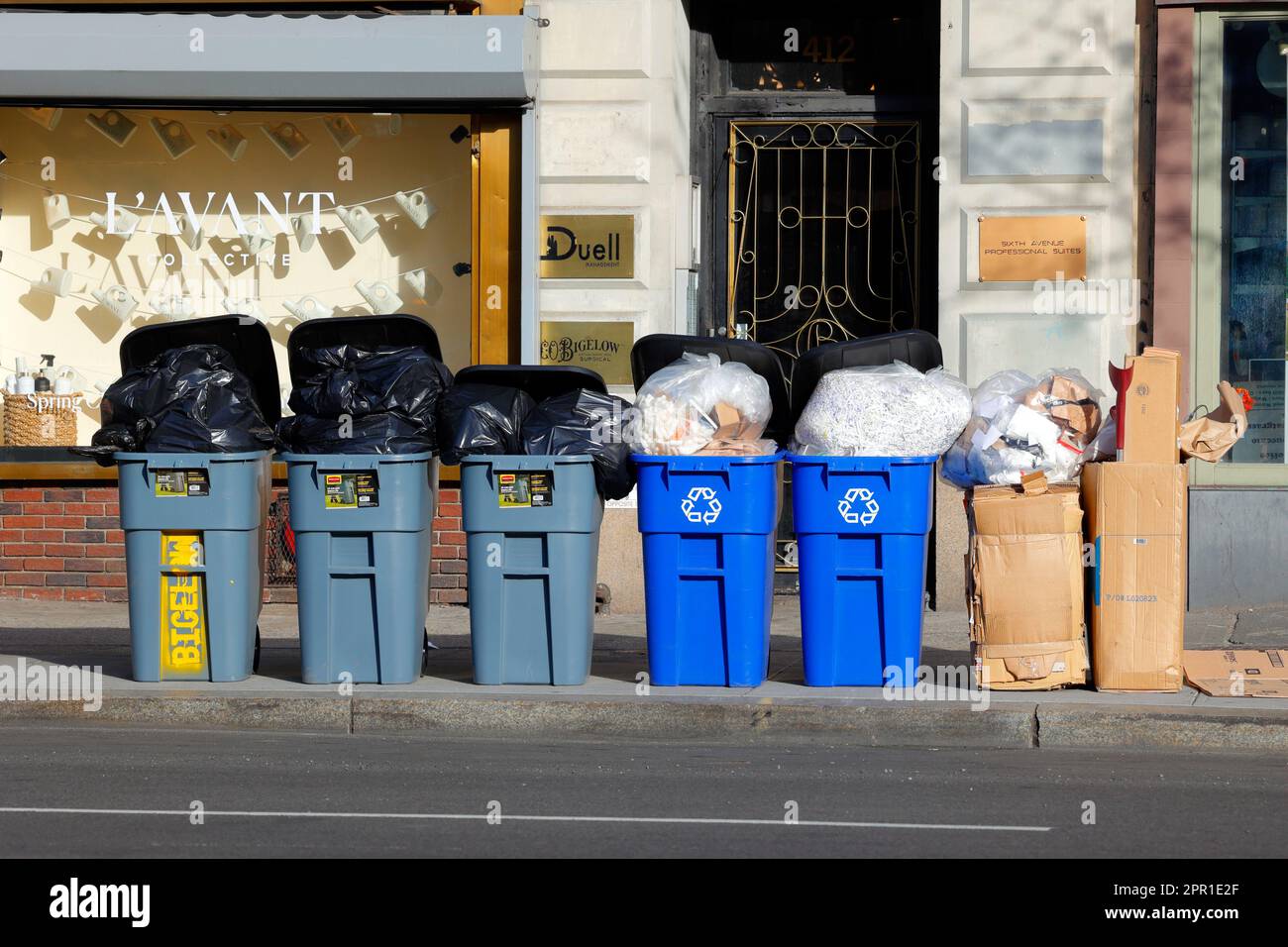 Kommerzieller Müll und Recycling werden ordentlich in Mülltonnen für die Abholung am Straßenrand vor der Apotheke Bigelow in New York City gelagert Stockfoto