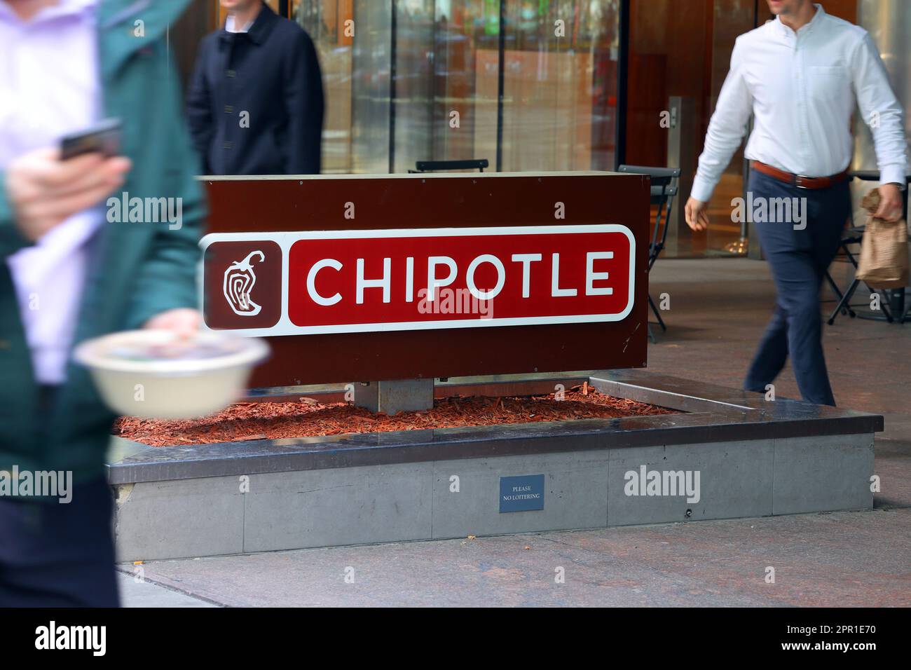 Büroangestellte mit Mittagessen zum Mitnehmen gehen an einem Chipotle in Midtown Manhattan, New York vorbei. Chipotle ist ein schnelles, zwangloses mexikanisches Restaurant Stockfoto