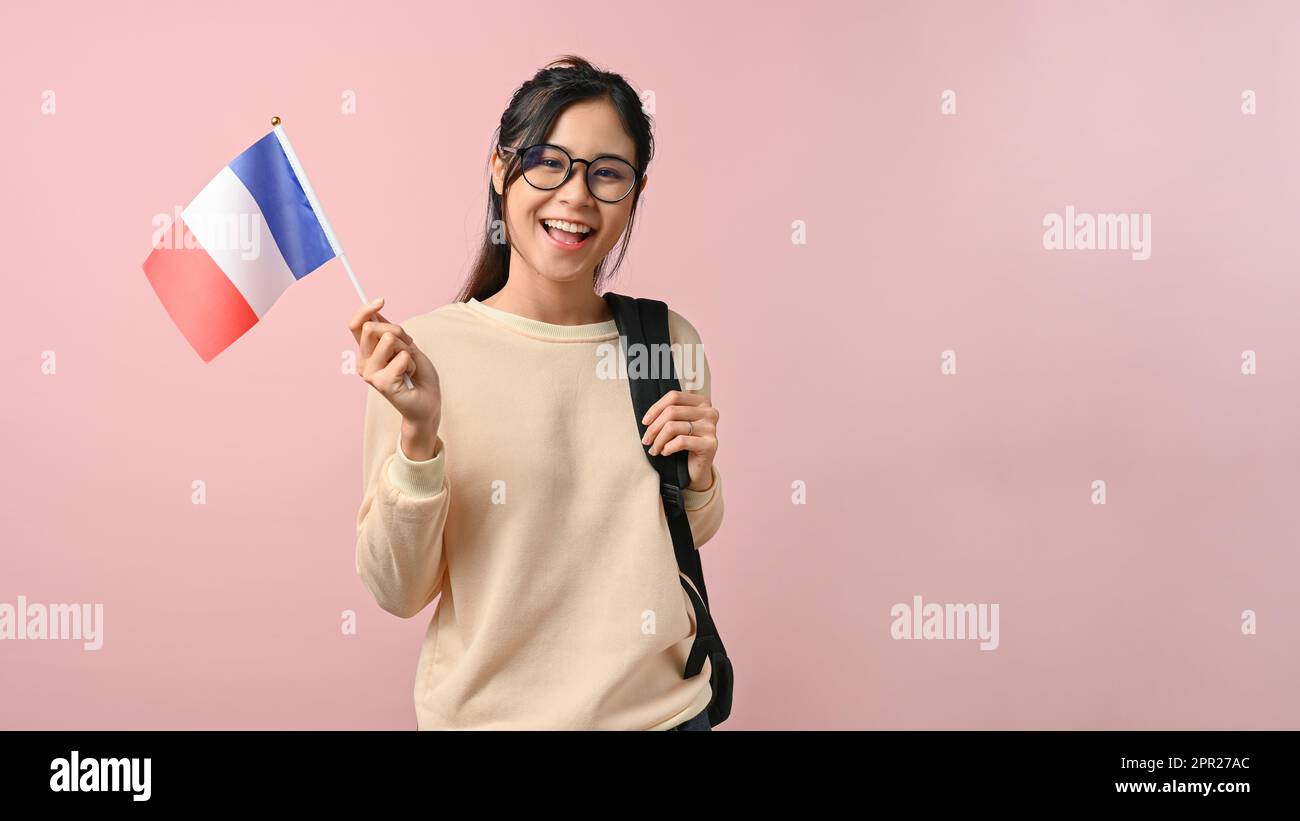 Fröhliches asiatisches Mädchen, das eine französische Flagge zeigt, auf pinkfarbenem isoliertem Hintergrund, Bildungskonzept. Studieren im Ausland Konzept. Stockfoto