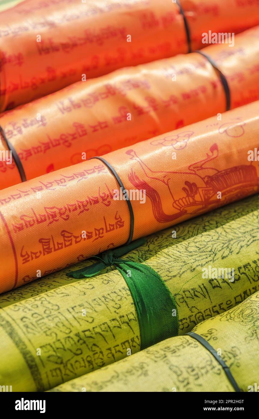 Aufgerollte Textilrollen mit kunstvoller tibetischer Sanskrit-Schrift und Illustrationen in lebhaften orangefarbenen und gelben Farben Stockfoto