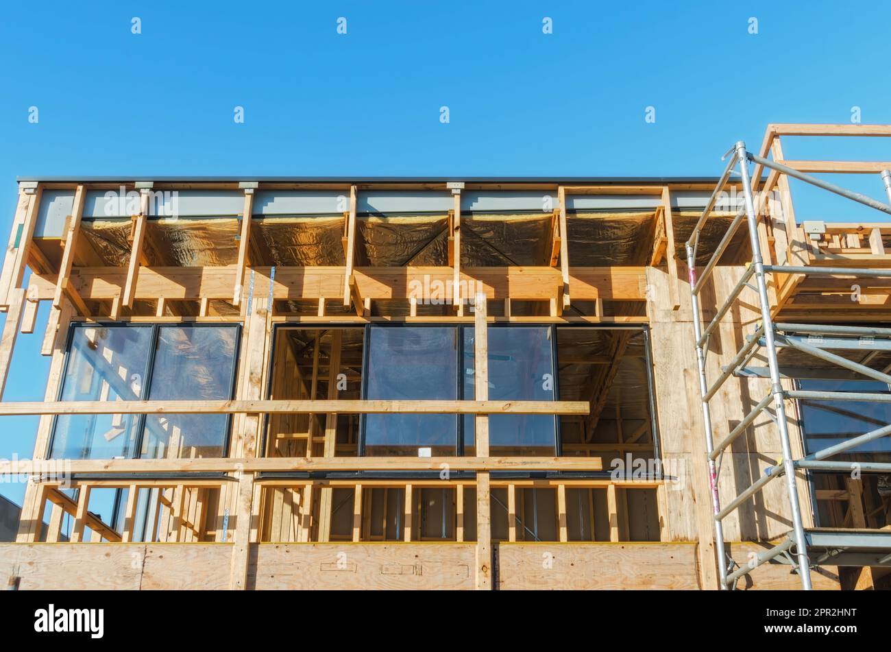 Ein Skelett-Holzhausrahmen in der frühen Bauphase, mit Balken und offenen Fensterräumen unter wolkenlosem Himmel Stockfoto