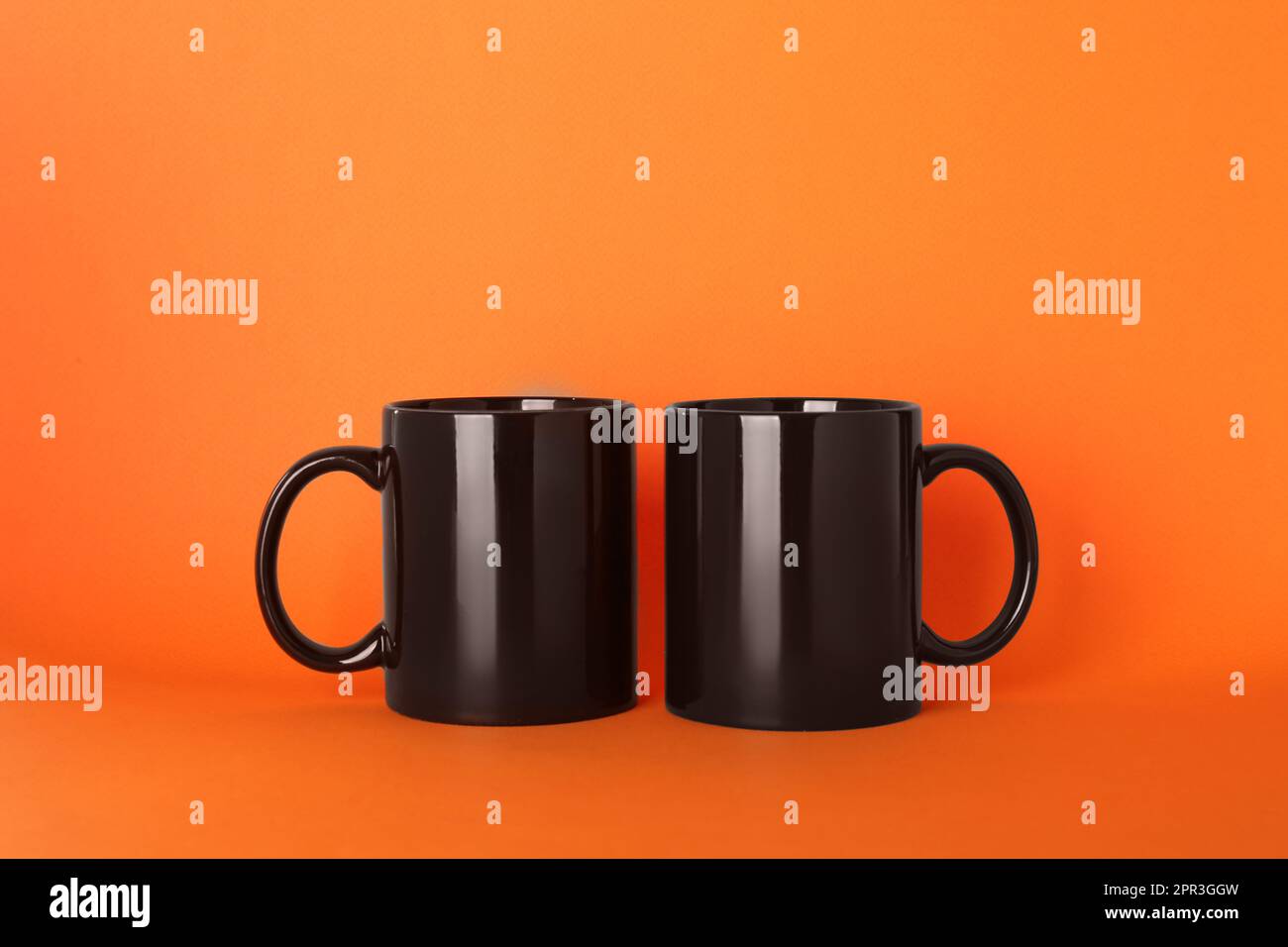 Leere schwarze Keramikbecher auf orangefarbenem Hintergrund Stockfoto