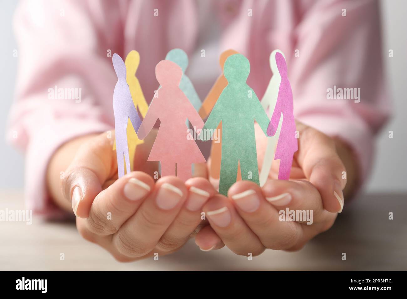 Eine Frau, die Papiermenschen am Tisch hält, Nahaufnahme. Diversitäts- und Integrationskonzept Stockfoto